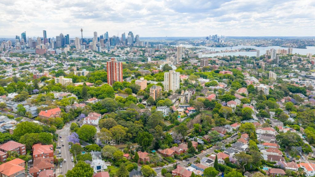 A stunning aerial view of Sydney, featuring the iconic Harbor Bridge and urban landscape filled with greenery.
